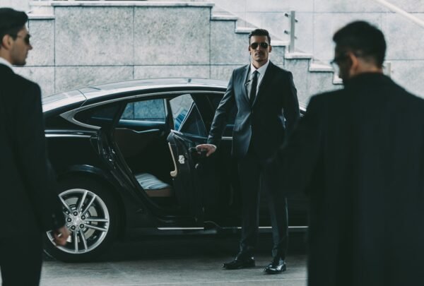 bodyguard-in-sunglasses-opening-car-door-to-businessman.jpg